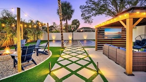 A well-lit outdoor patio area with a fire pit, seating, and a basketball court.