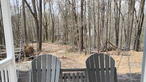A porch with two Adirondack chairs and a small table, surrounded by a wooden deck and a forest backdrop. - Briar Ridge Cabin in Osgood IN (Osgood)