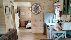 A wooden cabin interior with a plaid sofa, a wooden dining table, a kitchen area with a clock, and a bed in the background. - Briar Ridge Cabin in Osgood IN (Osgood)