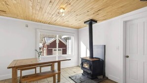 Une pièce avec une table en bois, un poêle à bois noir, une fenêtre et une porte.