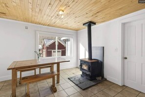 Una habitación con una mesa de madera, un estufa de leña negra, una ventana y una puerta.