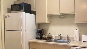 Cocina compacta con refrigerador, microondas, cafetera, lavaplatos y lavamanos.