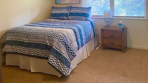 Un dormitorio con cama, ventilador de techo, mesita de noche y ventana con persianas.