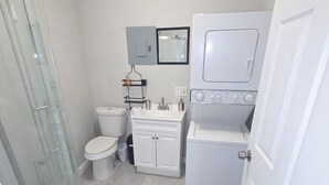 Un baño pequeño con cabina de ducha de vidrio, inodoro, lavabo con espejo y lavadora y secadora apiladas.
