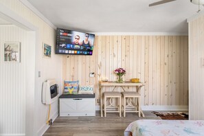 Ein Zimmer mit an der Wand montiertem Fernseher, einer Holzbank, einem kleinen Tisch mit Blumenvase und einem Bett mit floralem Überwurf.