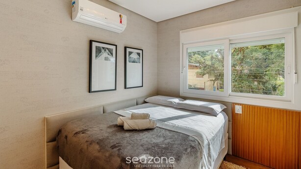 Un dormitorio con cama, equipo de aire acondicionado, cuadros enmarcados y ventana con vistas.