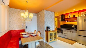 Una cocina compacta con electrodomésticos modernos, un comedor con sofá rojo y una araña.