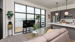 Ein modernes Wohnzimmer mit großem Fenster, einer Couch, einem Fernseher und einem kleinen Tisch mit einer Pflanze.