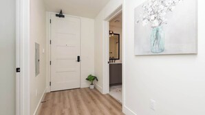 Ein Flur mit einer weißen Tür, einem kleinen Blumentopf und einem Gemälde einer Vase mit Blumen an der Wand.