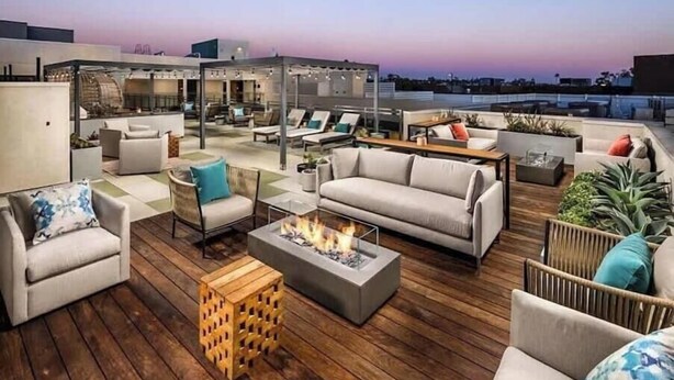 Eine Dachterrasse mit Sitzgelegenheiten im Freien, einer Feuerstelle und Blick auf die Skyline der Stadt.