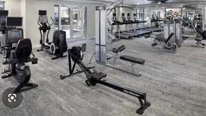 Ein Fitnessstudio mit verschiedenen Trainingsgeräten, darunter Laufbänder, Crosstrainer und Kraftgeräte.
