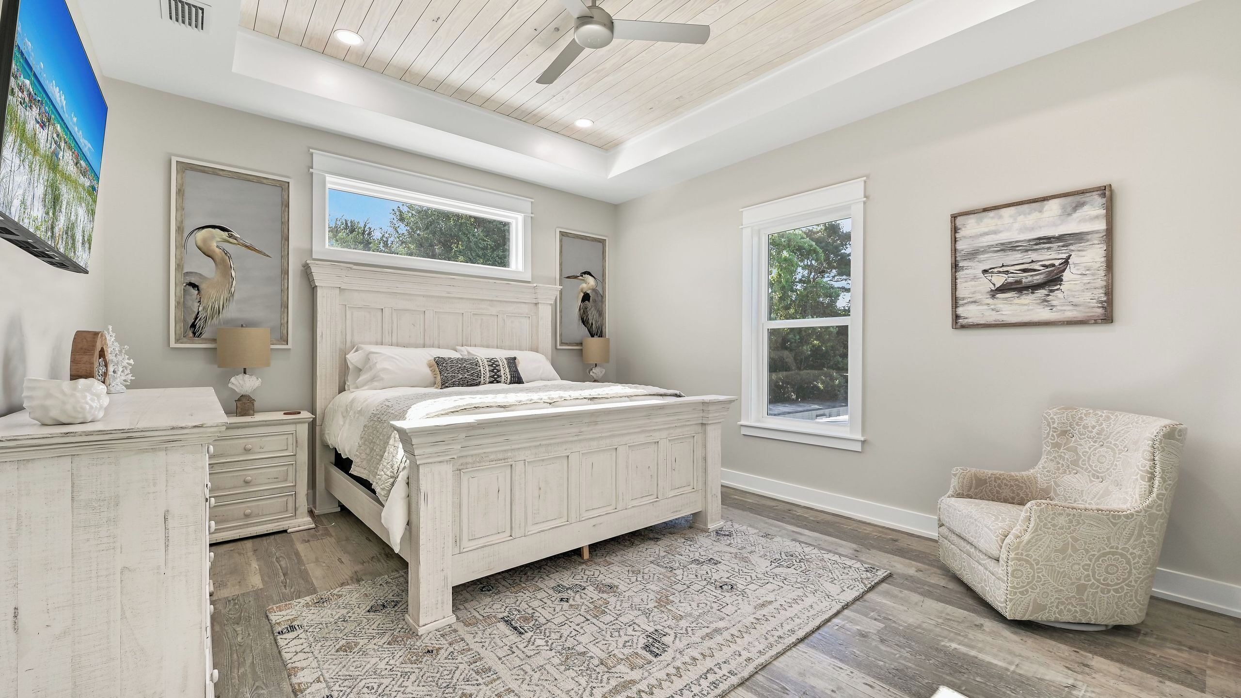 A bedroom with a large bed, two windows, a ceiling fan, and a chair.