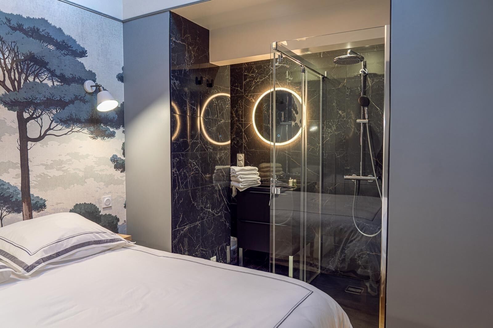 Een moderne hotelkamer met een bed, een douche met glazen wanden en een muur met een boommuurschildering.