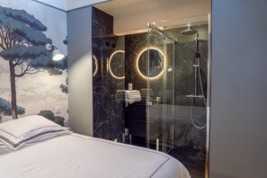 A modern hotel room with a bed, a shower with a glass enclosure, and a wall with a tree mural. - Charming Apartment in Montreuil-sur-Mer (Montreuil-sur-Mer)
