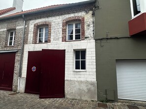 A building with two red garage doors, a brick facade, and a white wall with a garage door on the right. - Charming apartment in Montreuil sur mer (Montreuil-sur-Mer)
