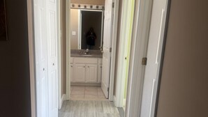 Een gang die leidt naar een badkamer met een wastafel en spiegel.