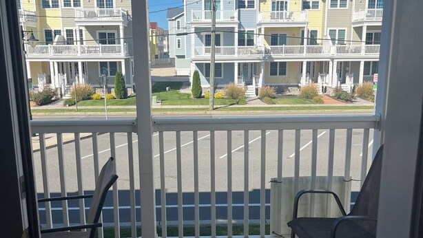 Een balkon met twee stoelen, uitzicht op meerverdiepinggebouwen, een parkeerplaats en een heldere blauwe lucht.