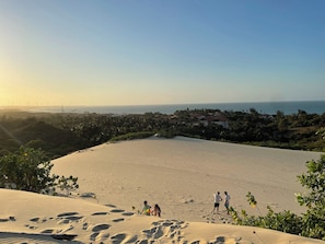 Wüstenlandschaft mit Sanddünen, einigen Personen und einer entfernten Ansicht einer Küstenstadt und des Ozeans.