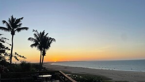 Een terras met buitenmeubilair met uitzicht op een strand bij zonsondergang.
