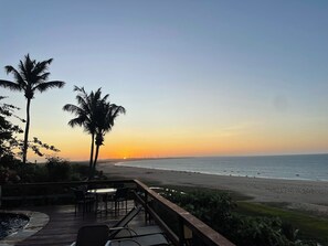 Eine Terrasse mit Sitzgelegenheiten mit Blick auf einen Strand bei Sonnenuntergang.
