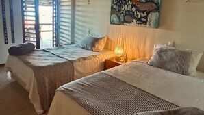 Een kamer met twee bedden, een schilderij aan de muur en een raam met zonwering.