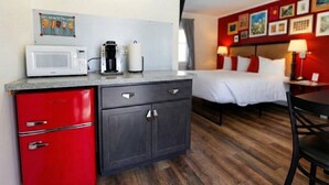 Une chambre d’hôtel compacte comprenant un coin cuisine, un lit, un espace repas et un mur décoré de tableaux encadrés.
