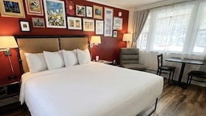 Une chambre d’hôtel avec un grand lit, un bureau, une chaise et des œuvres d’art accrochées aux murs.