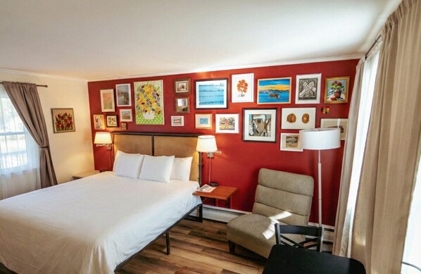 Habitación de hotel con una cama, una silla, un escritorio y una pared decorada con cuadros.