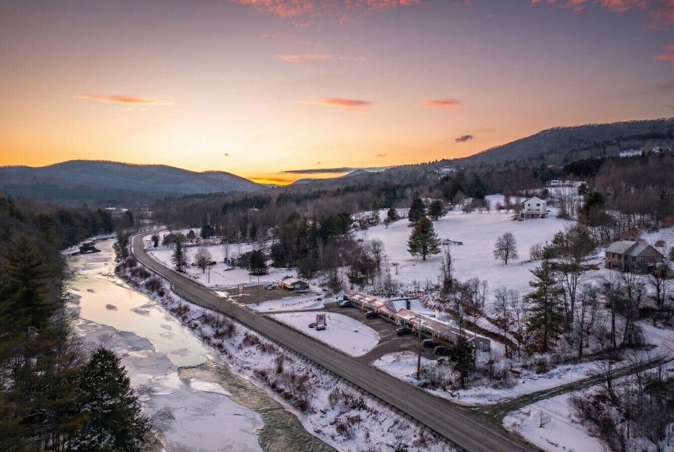 Paesaggio innevato con un fiume, una strada e degli edifici.
