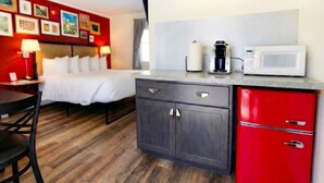 Une chambre d’hôtel compacte comprenant un lit, un petit bureau, une kitchenette équipée d’un four à micro-ondes et d’une machine à café, ainsi qu’un placard rouge.