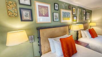 A hotel room with two beds, a headboard, wall-mounted lamps, and framed artwork on the wall.
