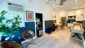 Ein modernes Wohnzimmer mit einer Couch, Sesseln, einem Couchtisch, einem Kamin und einer Küchenzeile im Hintergrund.