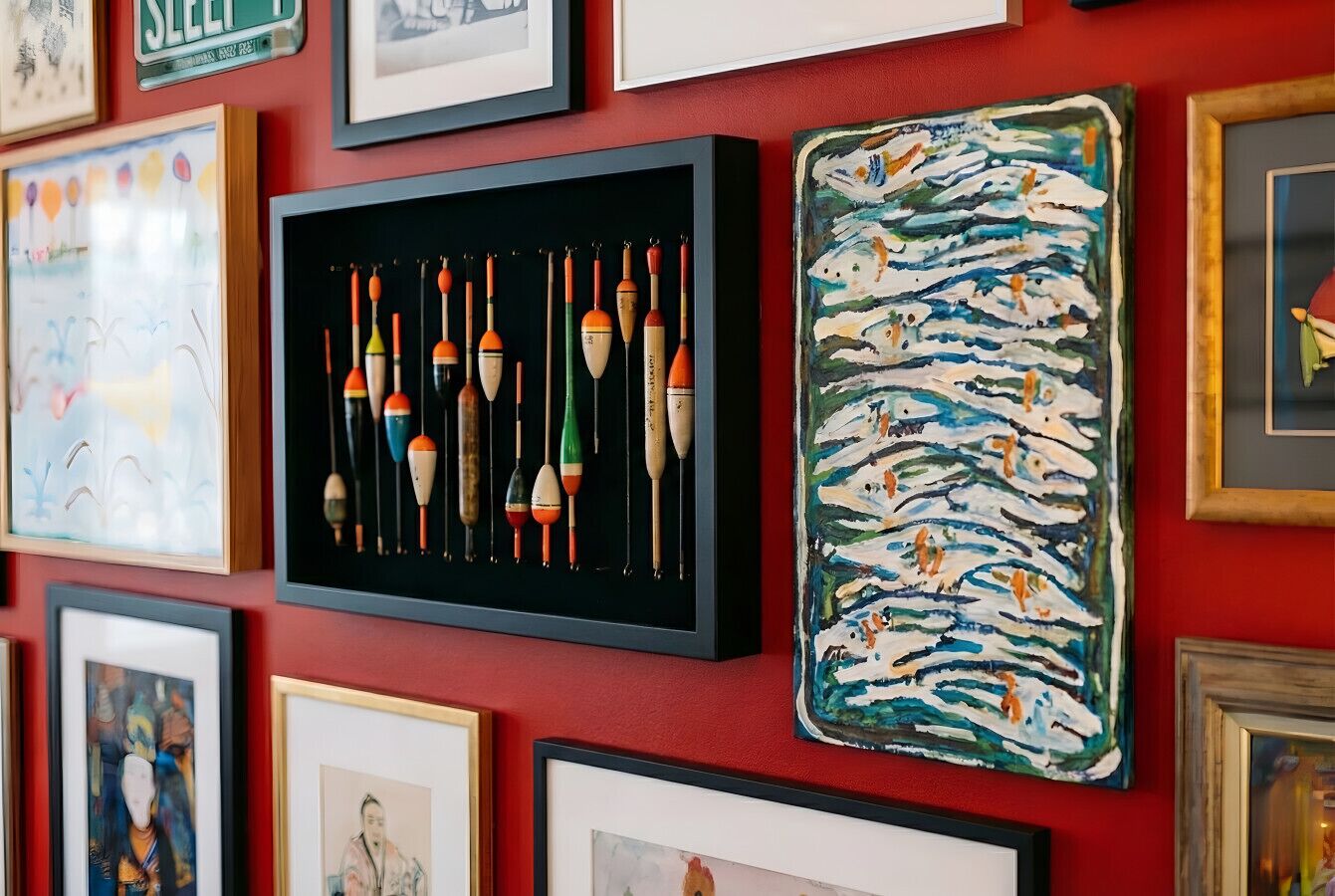A wall with various framed artworks, including a collection of fishing floats and a colorful abstract painting.