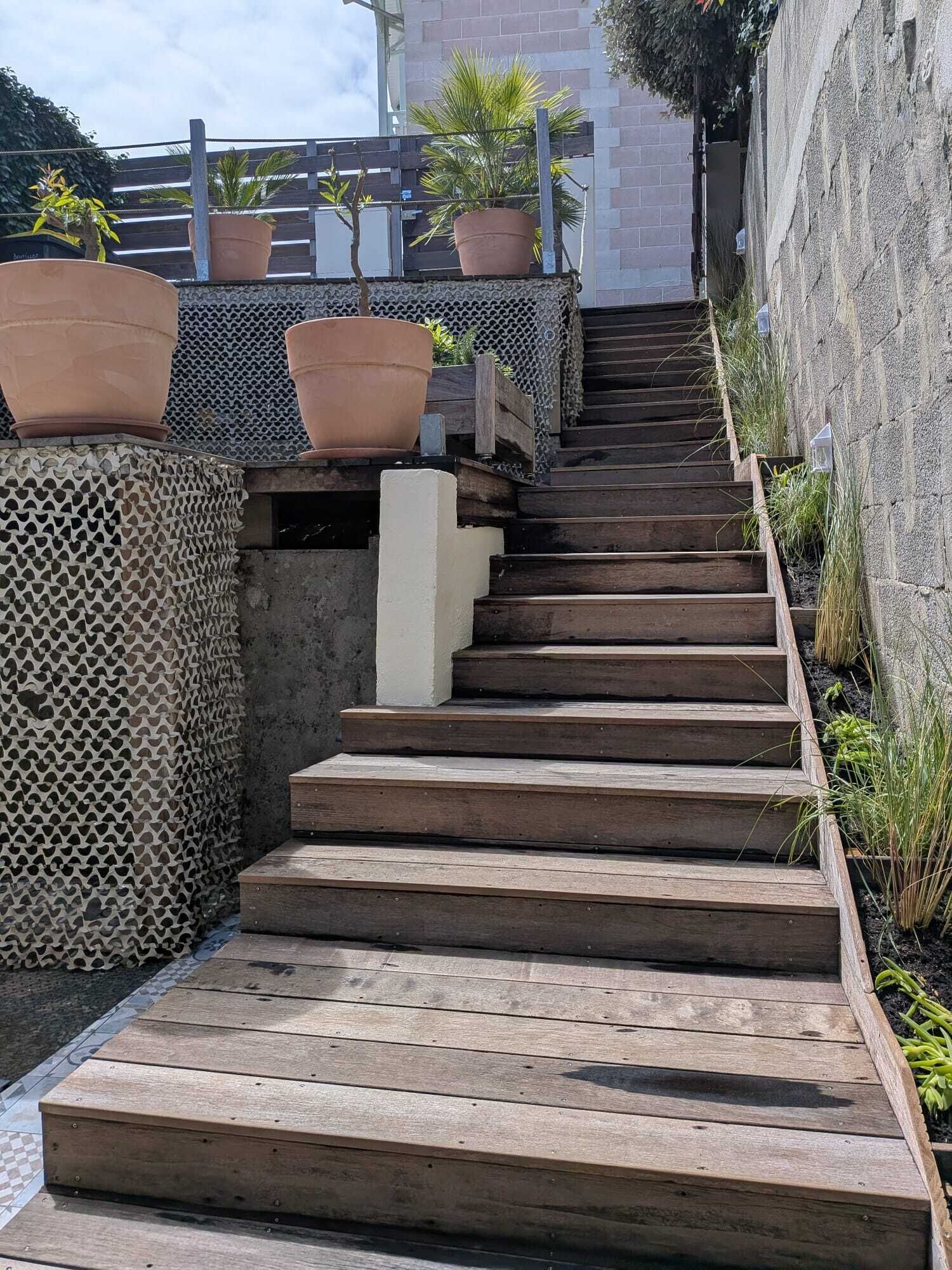A wooden staircase leading up to a terrace with potted plants and a stone wall.