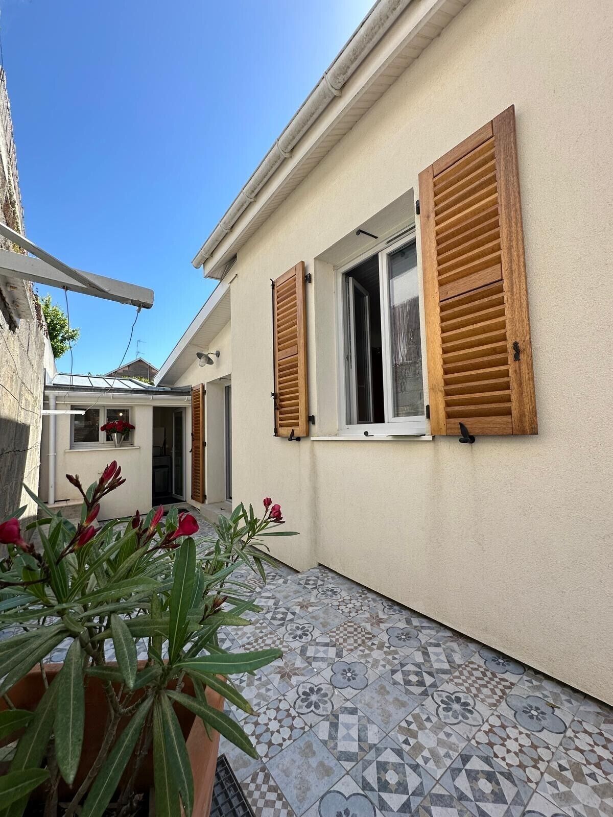 Un patio estrecho con suelo de baldosas, contraventanas de madera y macetas con plantas.