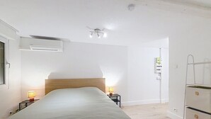 A bedroom with a bed, bedside lamps, an air conditioning unit, and a wardrobe. - Like a little house (Oberhausbergen)