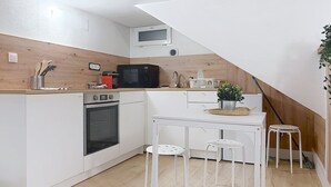 A compact kitchen with white cabinets, a microwave, an oven, and a small dining area with stools. - Like a little house (Oberhausbergen)
