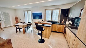 A modern kitchen with wooden cabinets, a black countertop, and a dining area with a table and chairs. - Nos Sweet Home - Red Rock suite Cozy mountain apartment (Dimaro)