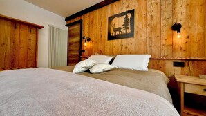 A wooden-paneled bedroom with a bed, two bedside tables, a radiator, and a wall-mounted light fixture. - Nos Sweet Home - Red Rock suite Cozy mountain apartment (Dimaro)