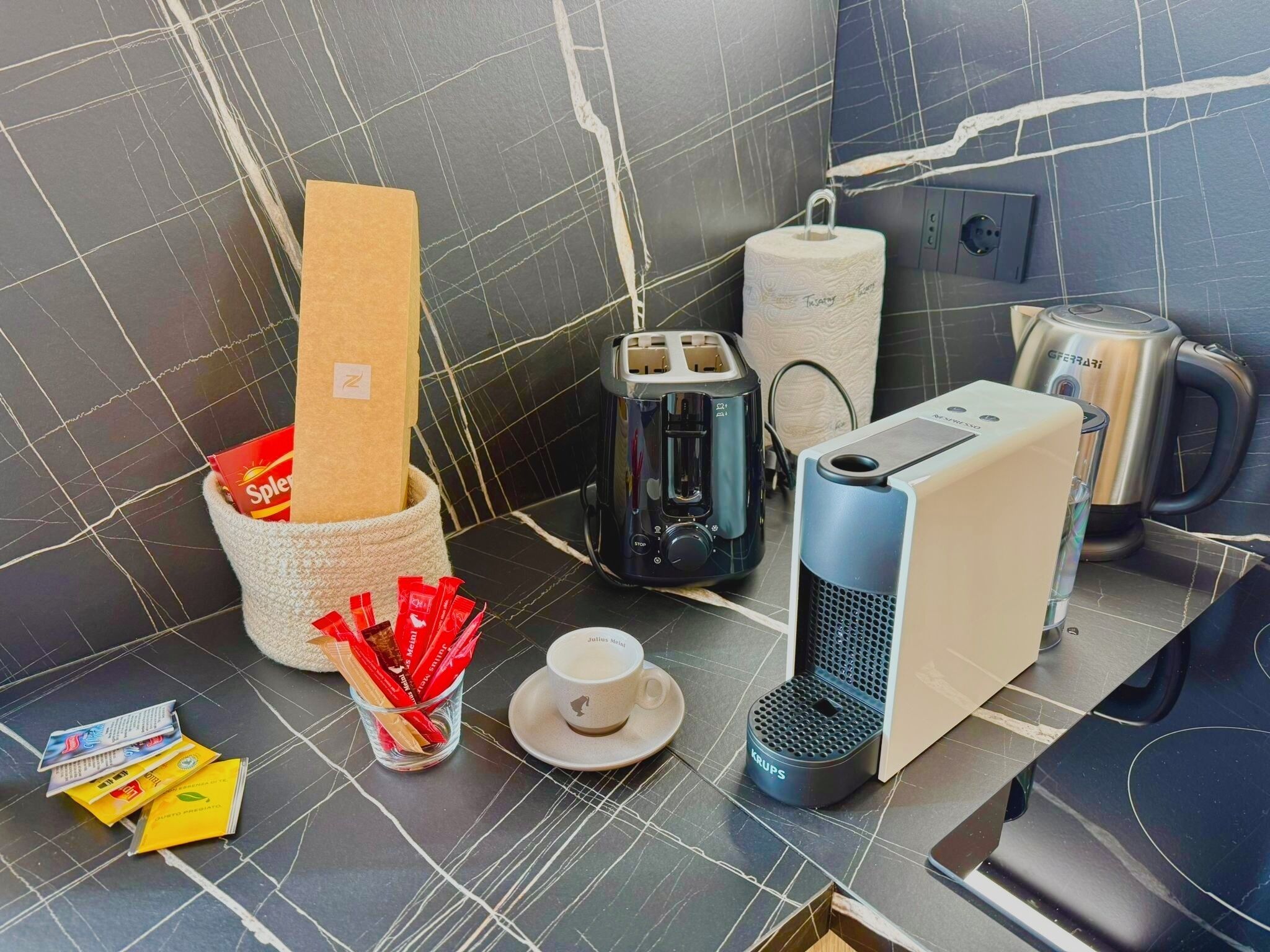 A kitchen counter with a toaster, kettle, coffee maker, and a cup of coffee.