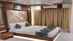 A modern bedroom with a large bed, a headboard, a nightstand, a mirror, and an air conditioning unit. - Hotel Anuha (Mira Bhayandar)