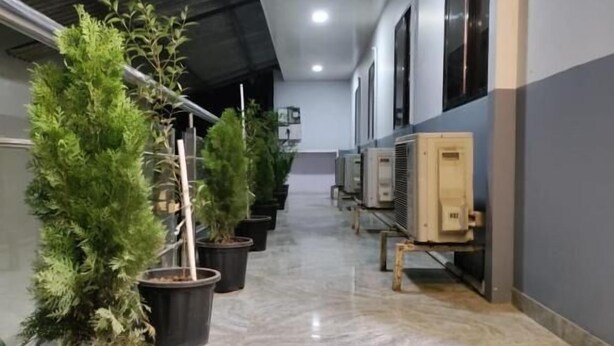 A corridor with potted plants, air conditioning units, and a tiled floor. - Hotel Anuha (Mira Bhayandar)