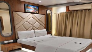 A modern bedroom with a large bed, a wooden headboard, a bedside table, and a wall-mounted mirror. - Hotel Anuha (Mira Bhayandar)