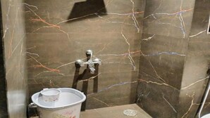 A shower with a marble wall, a handheld showerhead, and a bucket with a lid. - Hotel Anuha (Mira Bhayandar)