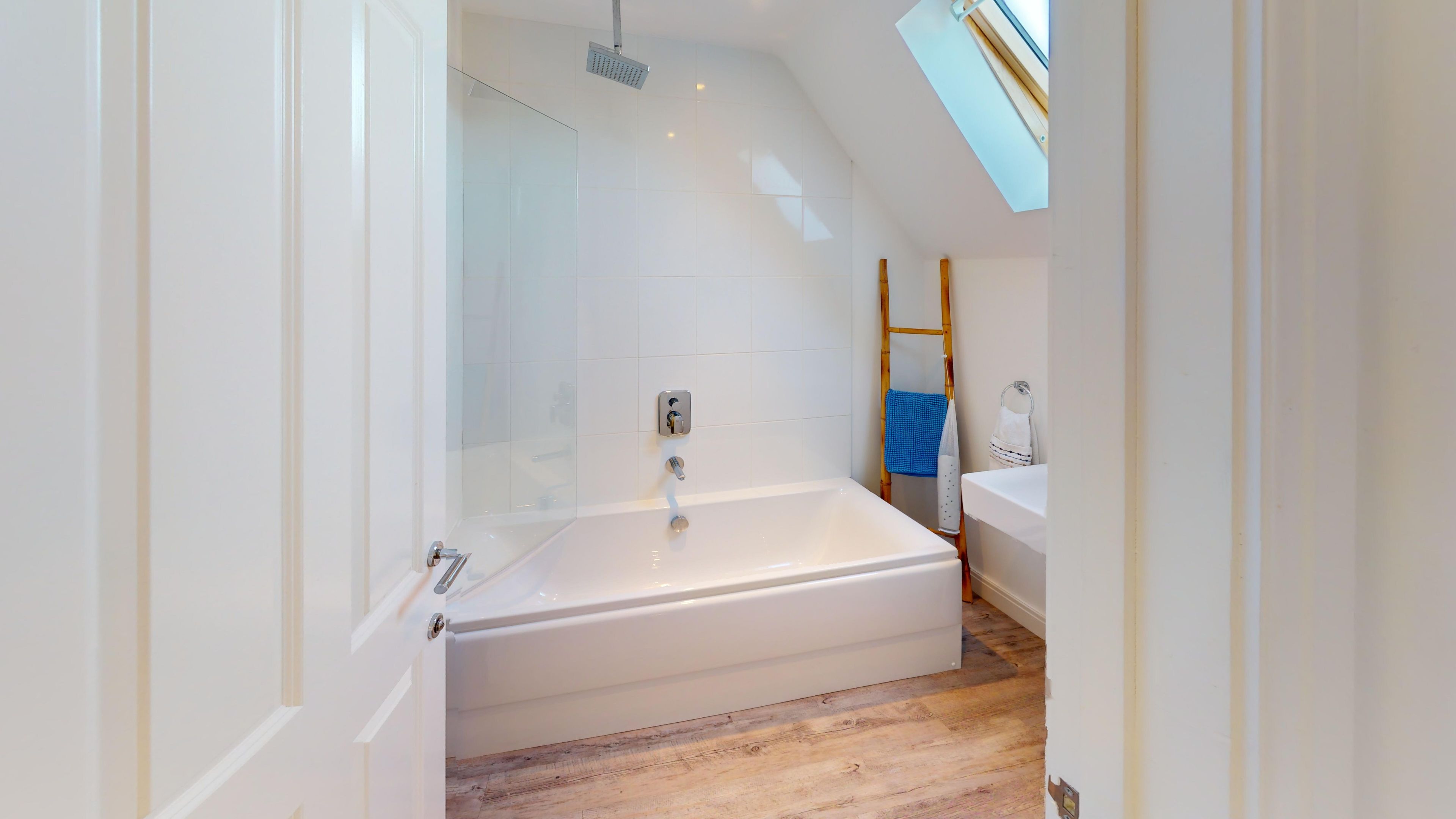 A modern bathroom with a glass shower enclosure, a white bathtub, and a wooden floor.