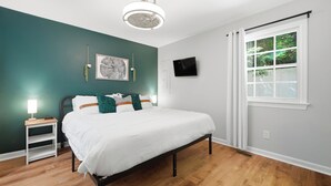 Une chambre à coucher comprenant un lit, une table de chevet, un téléviseur, une fenêtre avec des rideaux et un ventilateur de plafond.