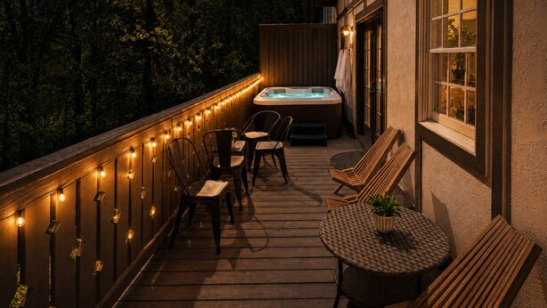 Une terrasse en bois avec un jacuzzi, des chaises et une table, le tout agrémenté de guirlandes lumineuses.