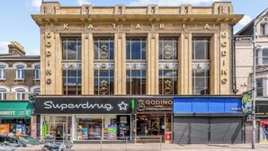 A building with 'KATAR' on the facade, a 'Superdrug' store, and a 'Godino Hotel' with a blue awning. - Stylish Studio with Balcony near Ilford Station (Ilford)