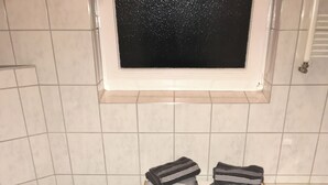 A bathroom with a toilet, a sink, a bathtub, and a shelf with folded towels. - Aparts House Essen (Essen)