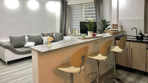 A modern kitchen with a central island, bar stools, a sofa, and a dining area. - Aparts House Essen (Essen)